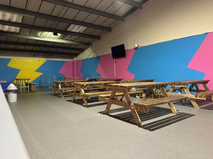Upstairs spectator seating area with picnic benches and a TV screen